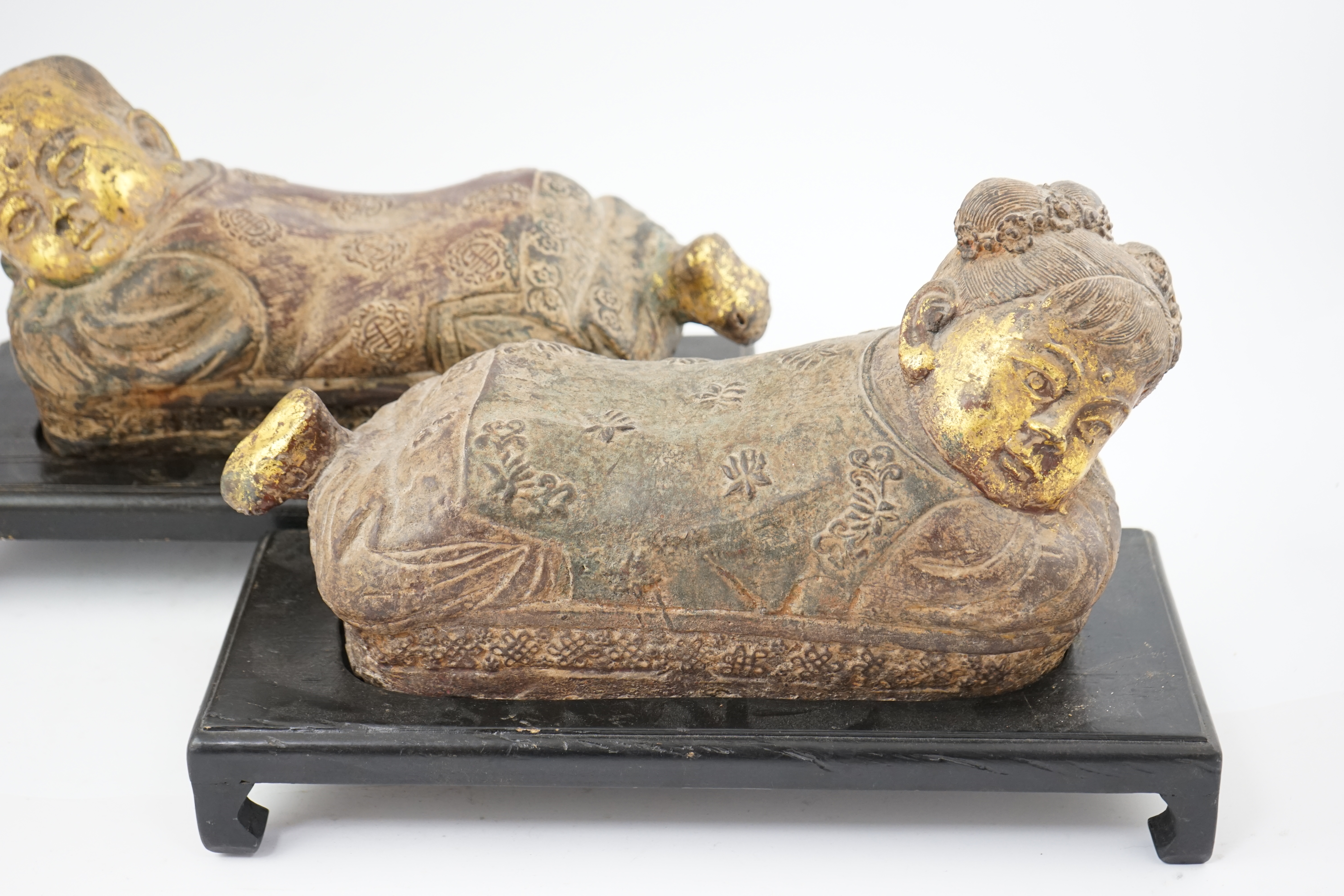 Two Chinese polychrome decorated iron pillows, modelled as sleeping children, on ebonised wood plinths, 44cm long. Condition - fair to good